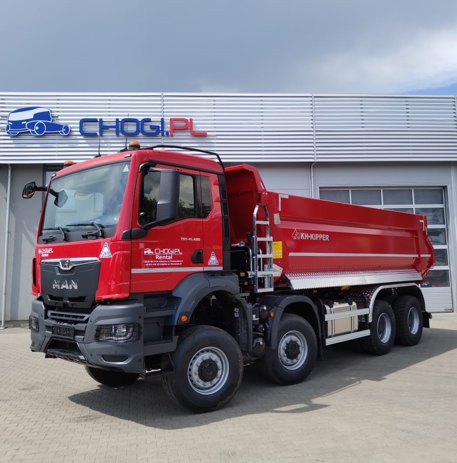 Czerwona ciężarówka MAN z zabudową KH-Kipper na tle budynku z logo CHOGI.PL Rental, widok z przodu z lekkiego ukosa.