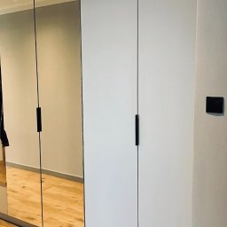 PPHU UNIZAR Adam Zarzycki - Nowoczesna szafa wnękowa z lustrzanymi drzwiami i minimalistycznymi, czarnymi uchwytami, oświetlenie sufitowe punktowe, widoczna drewnopodobna podłoga.