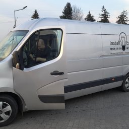 INSTALL EXPERT SPÓŁKA Z OGRANICZONĄ ODPOWIEDZIALNOŚCIĄ - Srebrny van firmy Install Expert z otwartymi drzwiami kierowcy, zaparkowany na kostce brukowej. Na boku logo i dane kontaktowe: instalacje, monitoring, alarm.