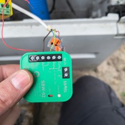 INSTALL EXPERT SPÓŁKA Z OGRANICZONĄ ODPOWIEDZIALNOŚCIĄ - Instalacja modułu WiFi Zamel SBW-02: zielony moduł z podłączonymi przewodami, widoczne złącza i oznaczenia, instalacja w trakcie podłączania.