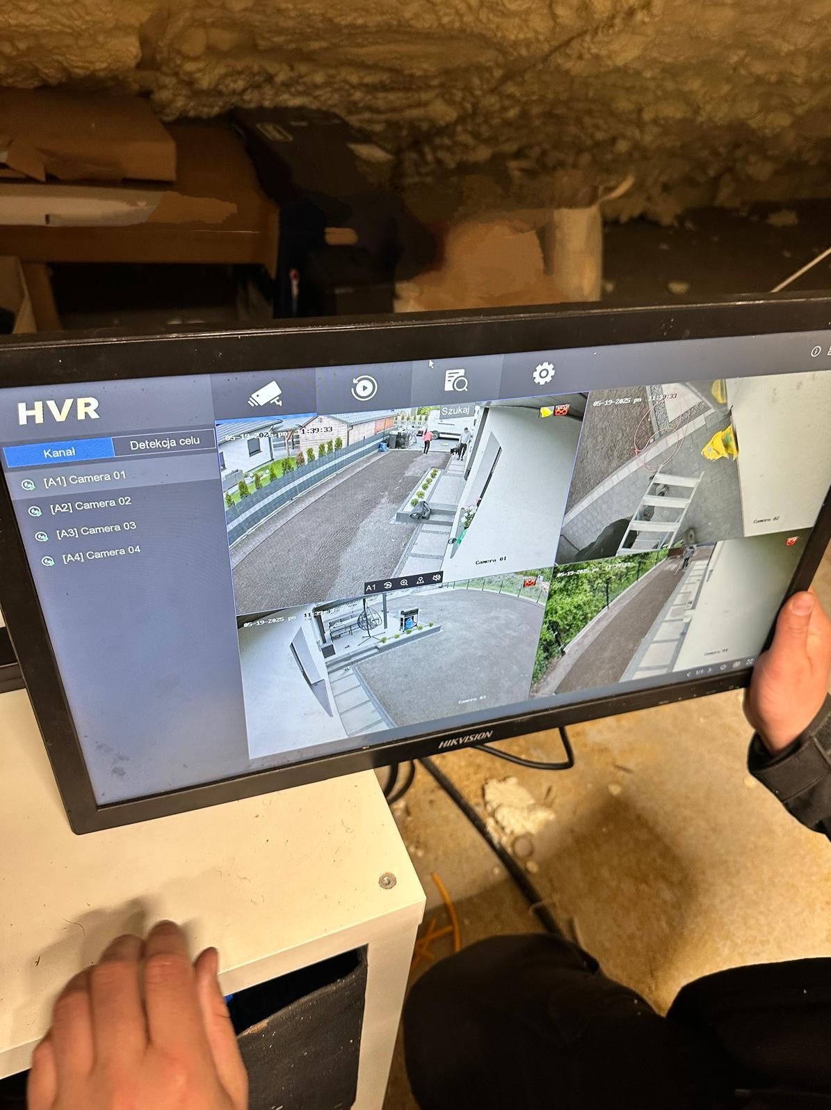 Ekran monitoringu HIKVISION z widokiem z czterech kamer na posesję, ukazujący podgląd na żywo z różnych perspektyw. Widoczne elementy to dom, ogród i podjazd.