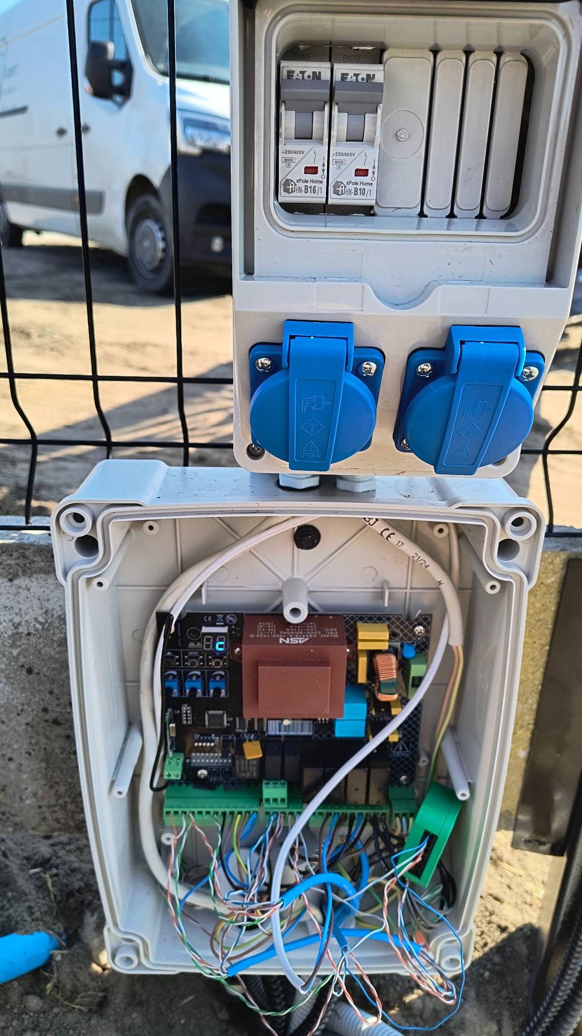 Rozdzielnica elektryczna zewnętrzna z dwoma gniazdami i wyłącznikami Eaton, zamontowana na ogrodzeniu, z widoczną wewnętrzną elektroniką i okablowaniem.