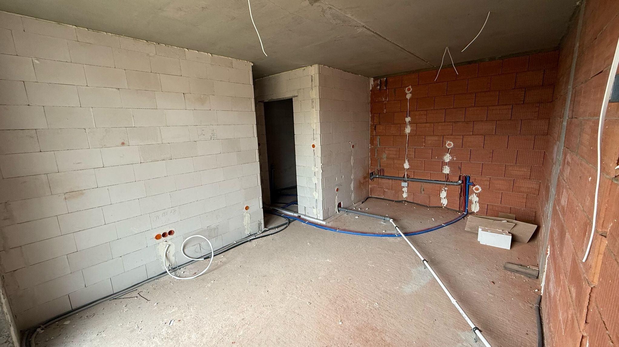 Wnętrze w trakcie prac instalacyjnych: widoczne przewody elektryczne i rury wodne na tle surowych ścian z bloczków i cegły. Nowe instalacje w budynku w stanie deweloperskim.