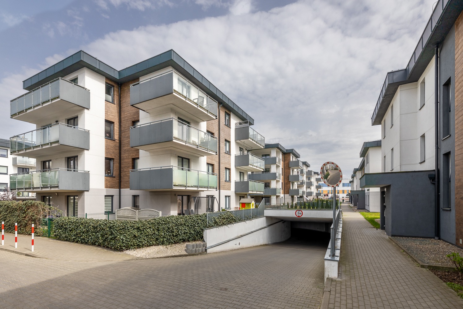 Nowoczesne budynki mieszkalne z balkonami i podziemnym parkingiem, widok z poziomu ulicy, znak ograniczenia wysokości wjazdu.