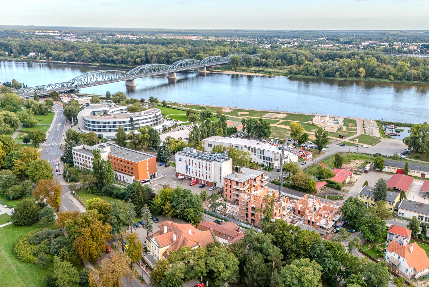 Panorama miasta z lotu ptaka, widoczny most stalowy nad rzeką, budynki hotelowe i budowa w toku.