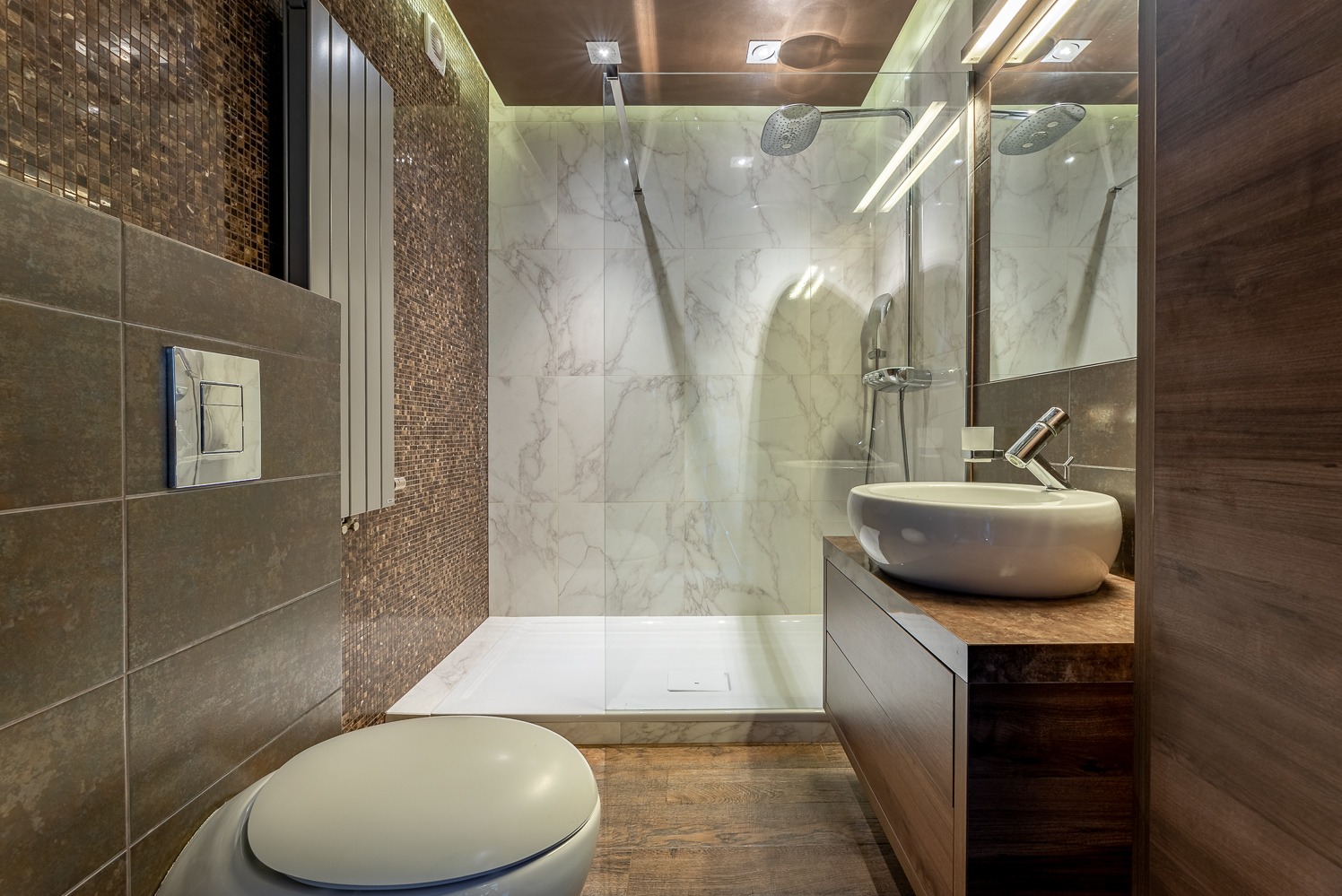 Nowoczesna łazienka z kabiną prysznicową walk-in, umywalką nablatową na drewnianej szafce i toaletą w kolorach brązu, bieli i szarości.