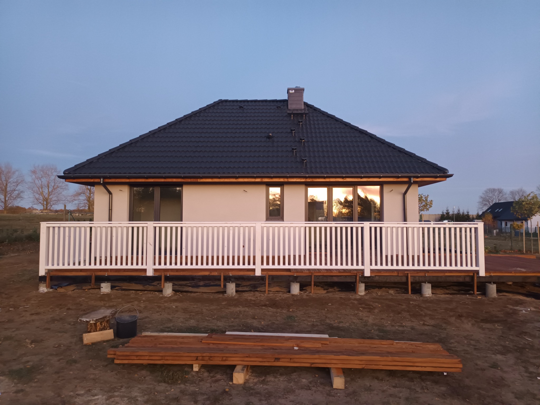 Dom jednorodzinny z nowo wybudowanym tarasem z białymi balustradami, widoczne deski i elementy konstrukcyjne w trakcie budowy.
