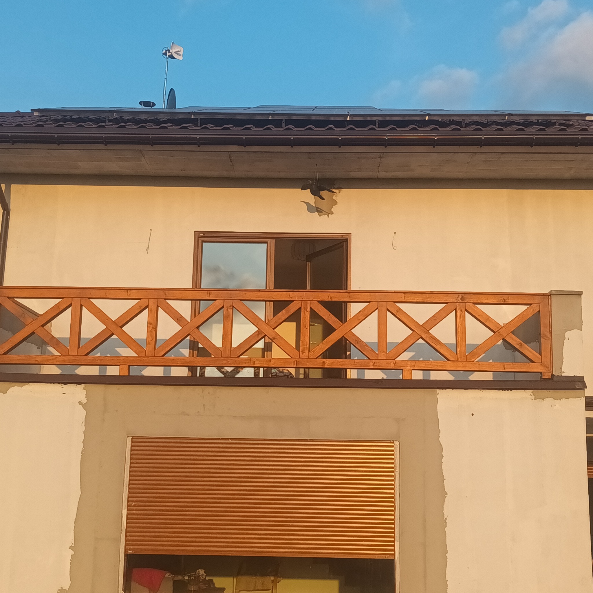 Balkon z drewnianą balustradą o krzyżowym wzorze, widok z dołu na elewację budynku z widocznymi śladami prac wykończeniowych.