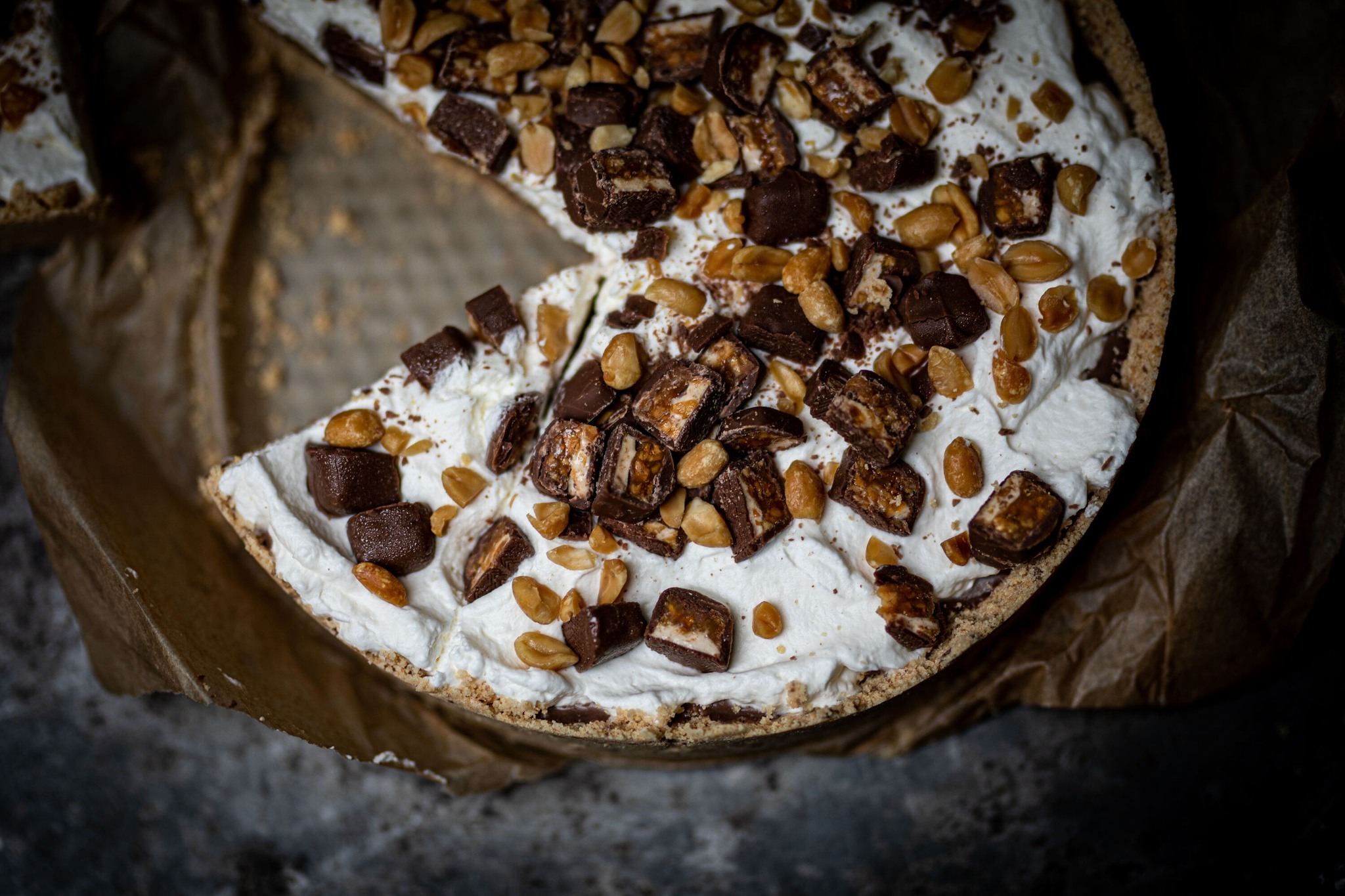 Kawałek tortu z kremem, orzechami i kawałkami batoników czekoladowych, ułożony na papierze do pieczenia, widok z góry.