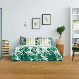 Jasna, drewnopodobna podłoga w sypialni z łóżkiem, zielonym fotelem i białym regałem, oświetlona naturalnym światłem.