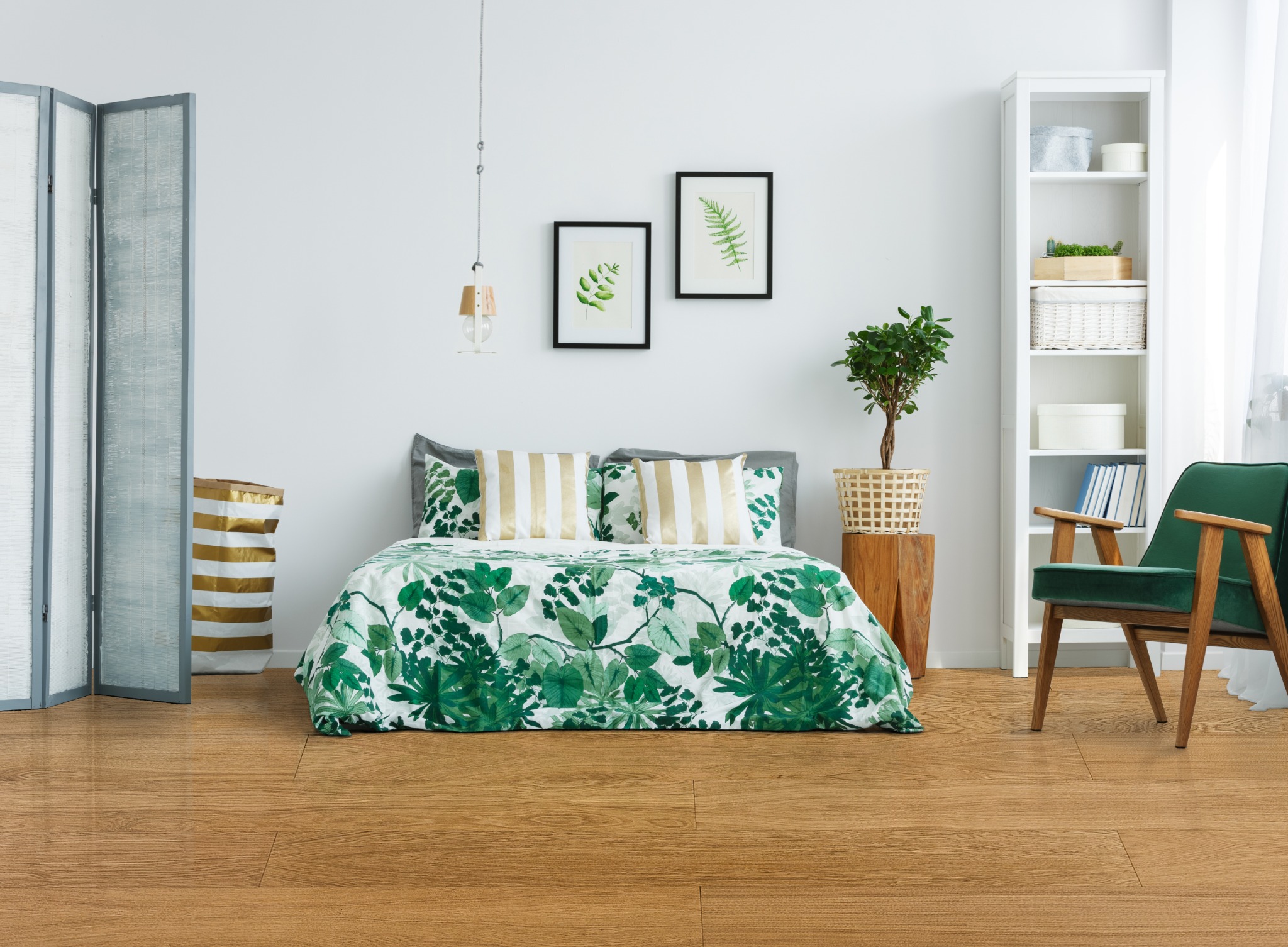 Jasna, drewnopodobna podłoga w sypialni z łóżkiem, zielonym fotelem i białym regałem, oświetlona naturalnym światłem.