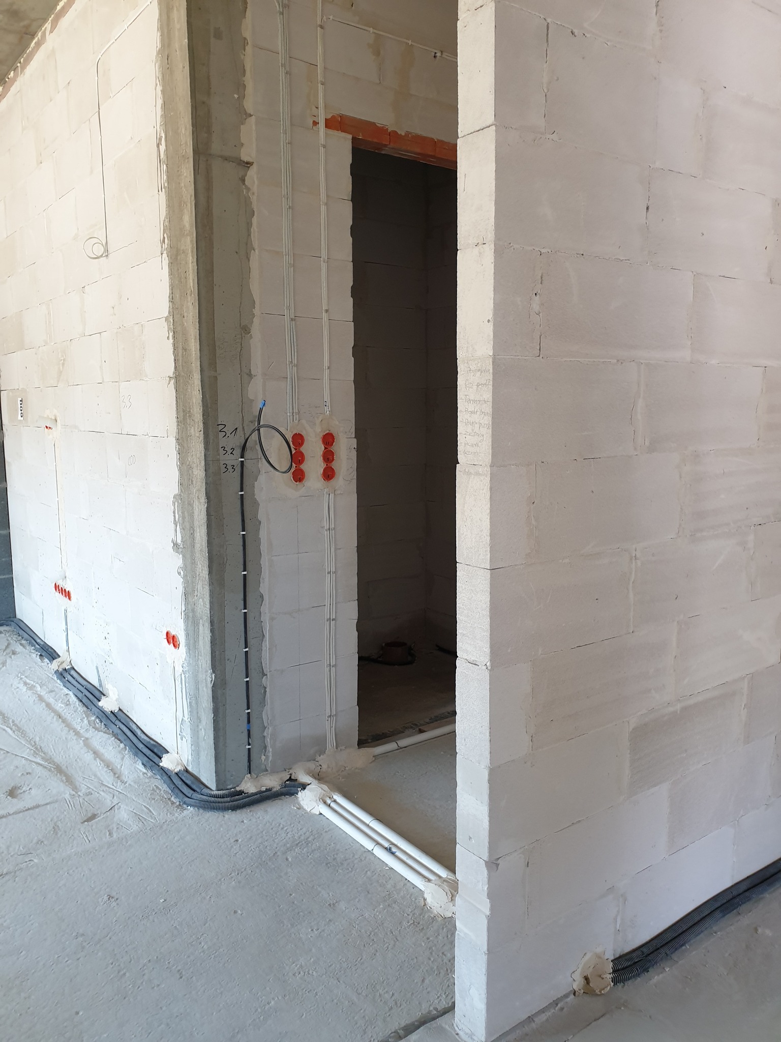 Surowy stan budynku w trakcie rozprowadzania instalacji elektrycznej: widoczne kable w peszlach mocowane do ściany z betonu komórkowego, puszki pod gniazdka.