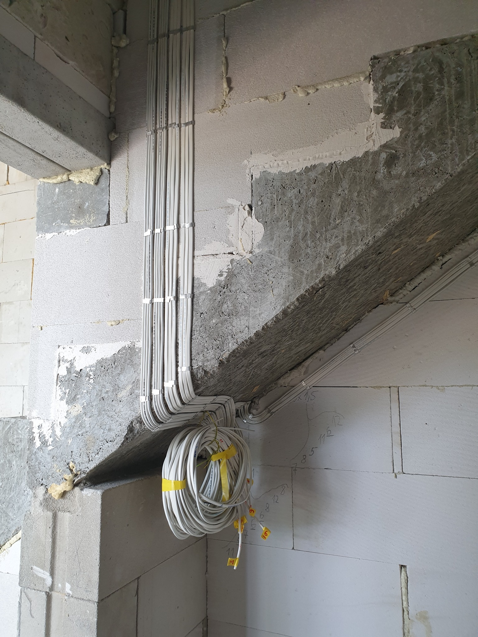 Nowa instalacja elektryczna w surowym stanie budynku w Toruniu, z widocznymi kablami prowadzonymi wzdłuż betonowej belki, zabezpieczone żółtą taśmą.