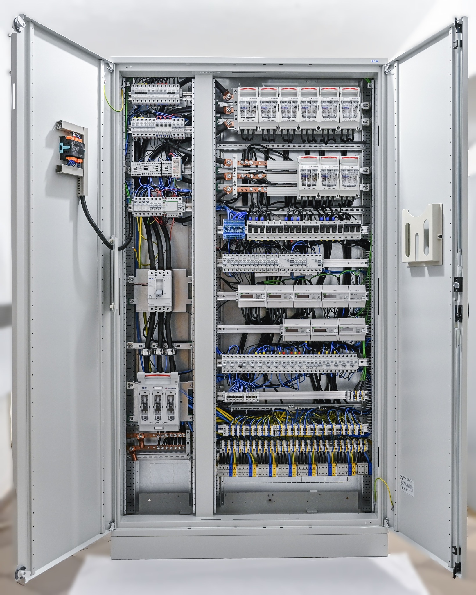 Otwarta szafa elektryczna z widocznymi bezpiecznikami, przewodami i elementami łączeniowymi, starannie ułożonymi wewnątrz obudowy.