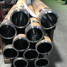 Stos rur po obróbce w Tarnowskich Górach, widoczne ślady rdzy i metaliczne wnętrze, ułożone na drewnianym stojaku w hali.