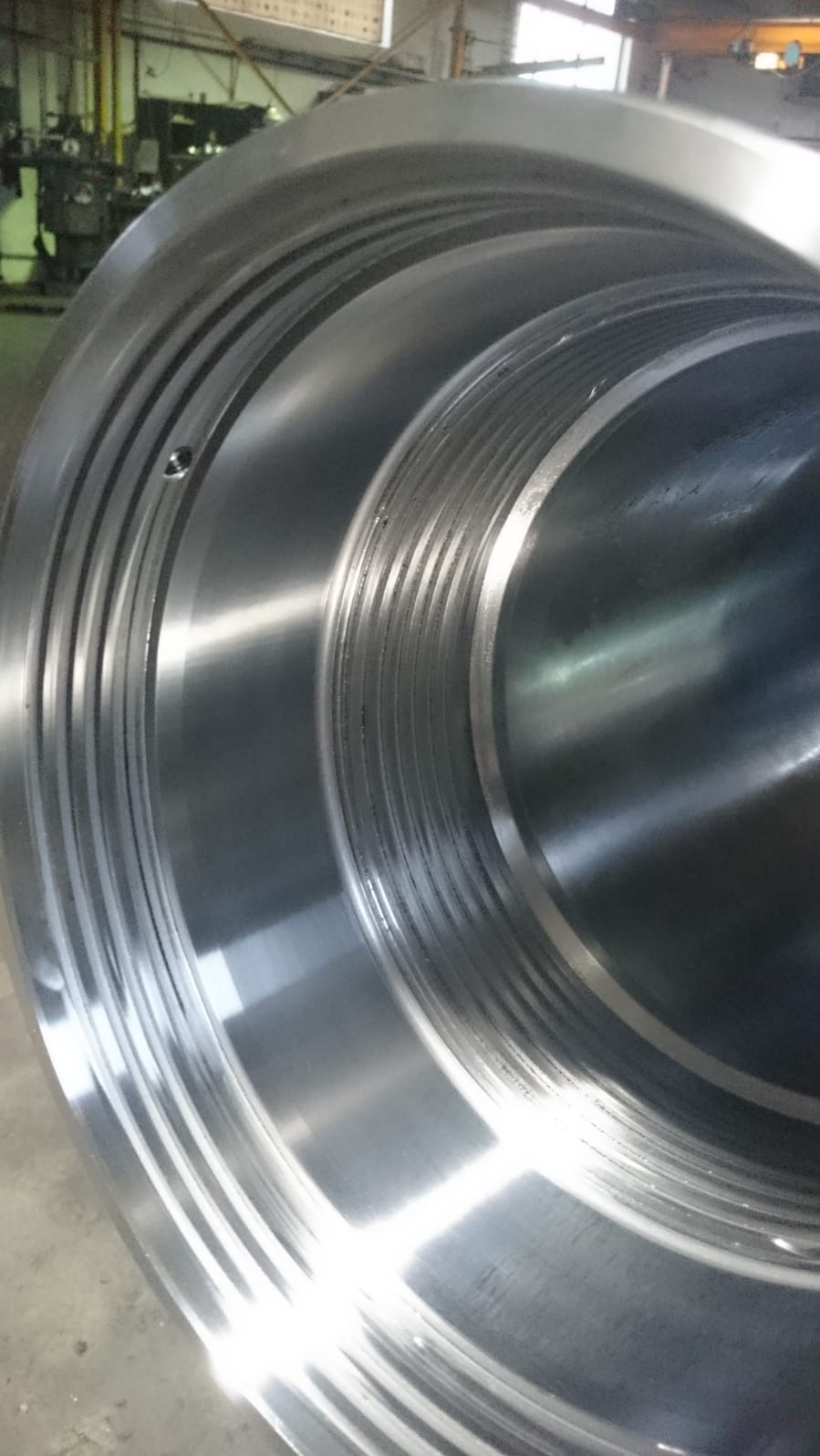 Wnętrze metalowego cylindra z precyzyjnymi, koncentrycznymi rowkami, widoczne ślady obróbki skrawaniem i niewielki otwór.