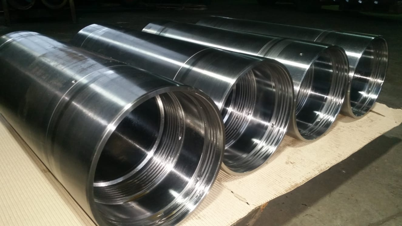 Rząd polerowanych, metalowych tulei z wewnętrznym gwintem, ułożonych na tekturze, widoczne ślady obróbki skrawaniem.