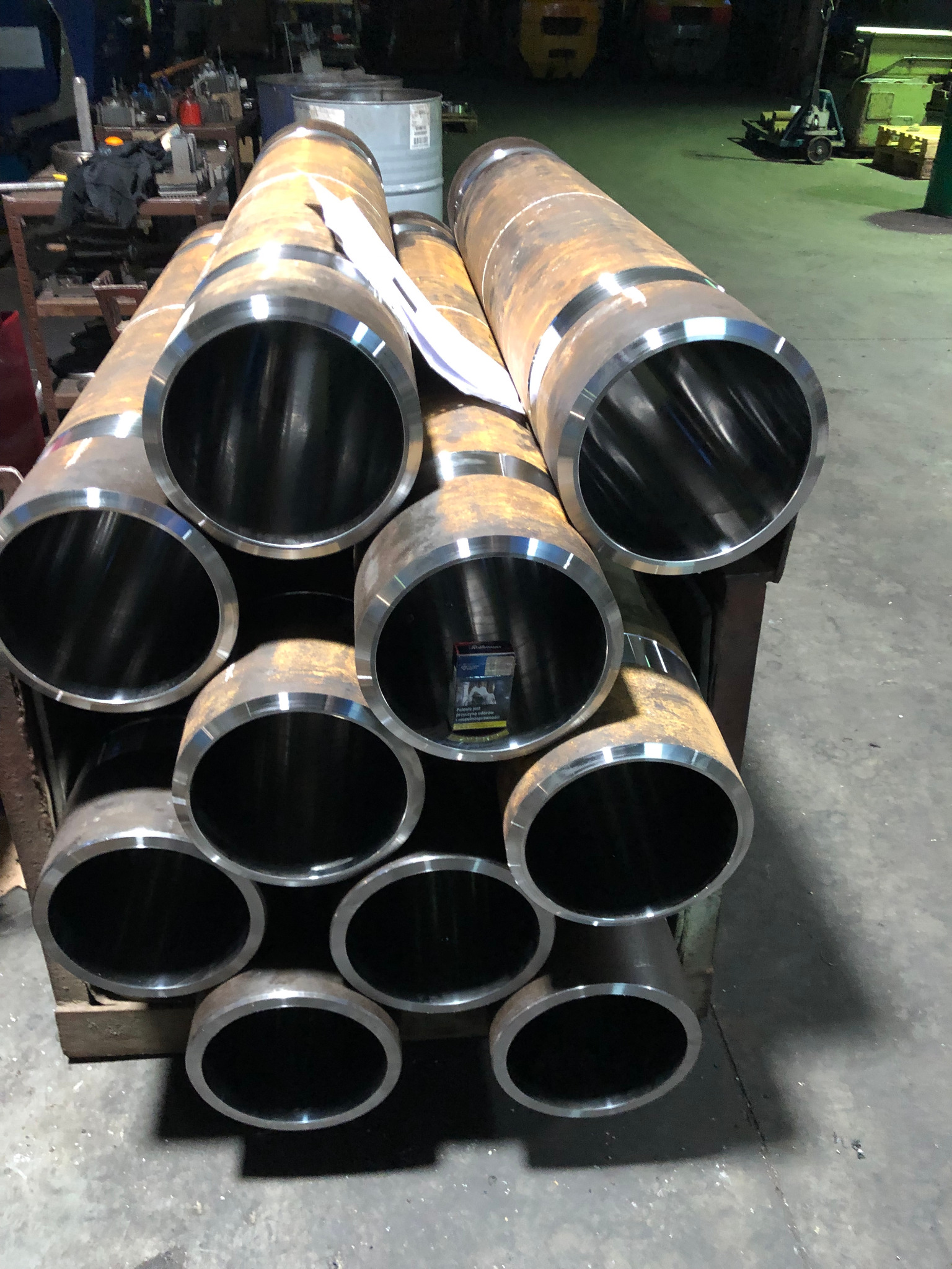 Stos rur po obróbce w Tarnowskich Górach, widoczne ślady rdzy i metaliczne wnętrze, ułożone na drewnianym stojaku w hali.