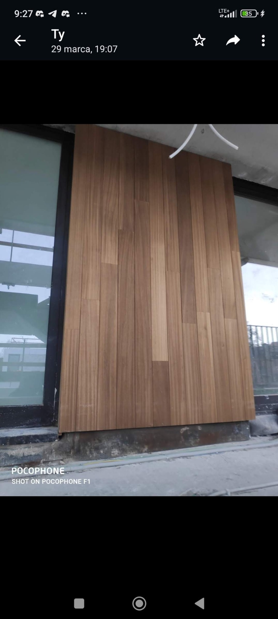 Montaż drewnianej okładziny ściennej z desek na ścianie przy oknie, widoczne kable pod sufitem i surowy stan wykończenia podłogi.