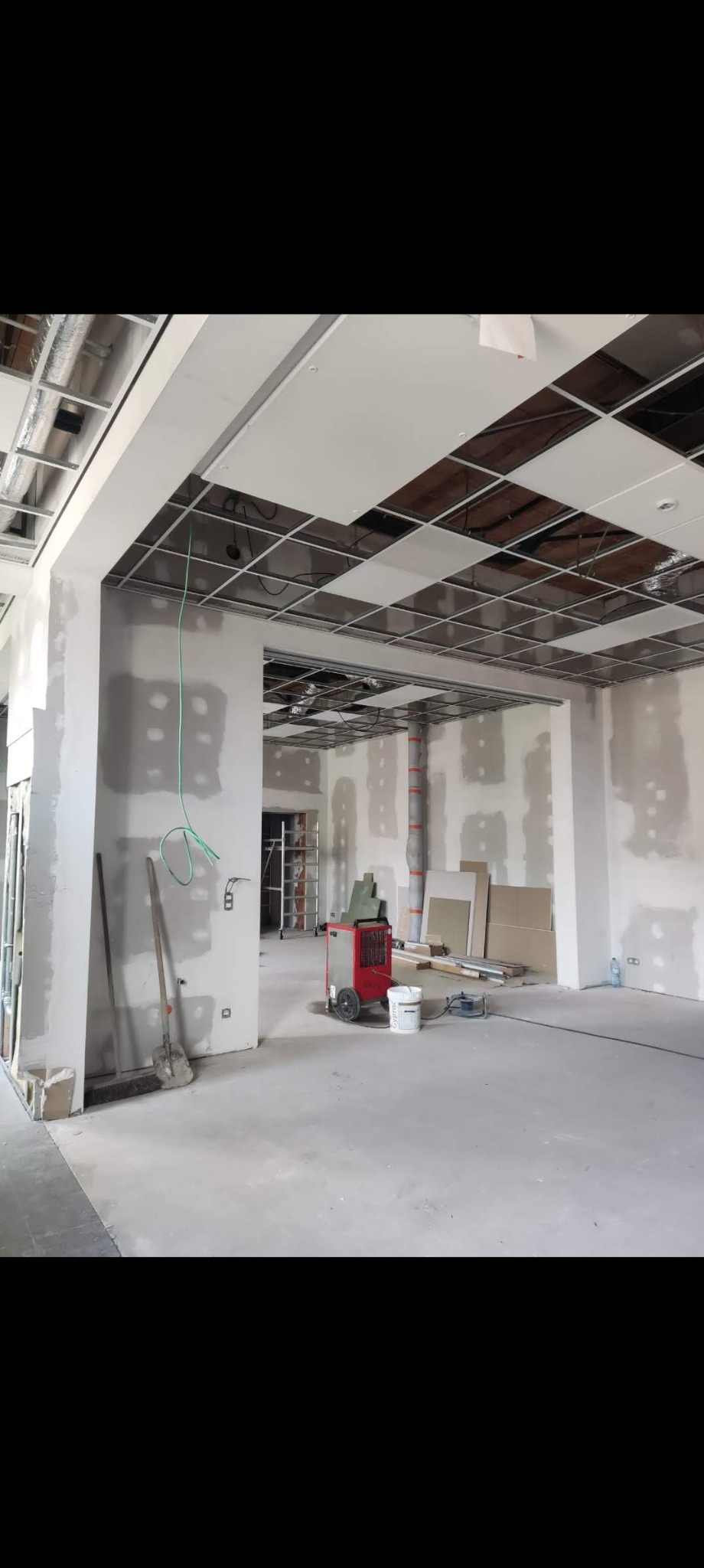 Wnętrze biura w trakcie prac wykończeniowych: ściany przygotowane do malowania, częściowo zamontowany sufit podwieszany, widoczny agregat grzewczy i narzędzia.