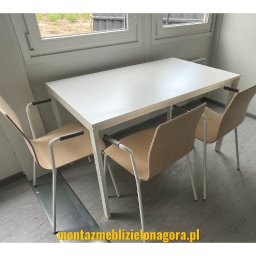 Montaż mebli Zielona Góra - Biały stół z czterema krzesłami z podłokietnikami w minimalistycznym biurze, widok z boku, pod oknem.