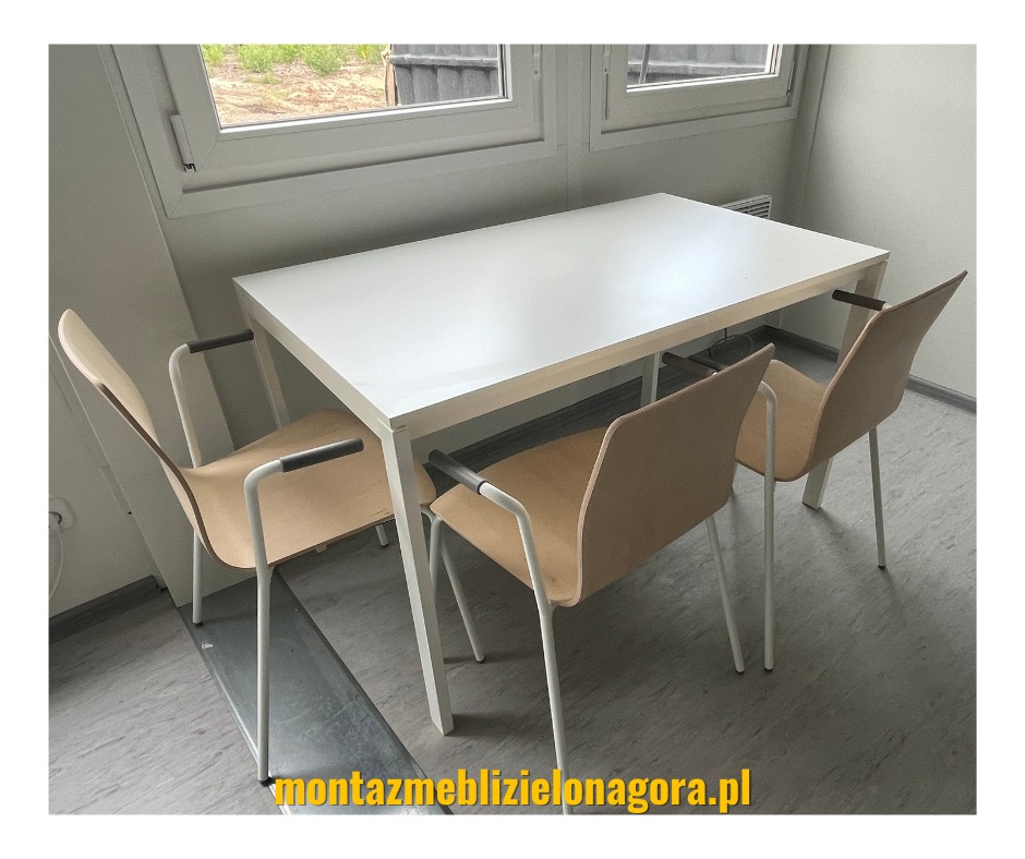 Biały stół z czterema krzesłami z podłokietnikami w minimalistycznym biurze, widok z boku, pod oknem.