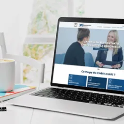 Laptop wyświetlający stronę internetową firmy z branży nieruchomości na biurku z kawą i notatnikiem w jasnym, minimalistycznym otoczeniu.