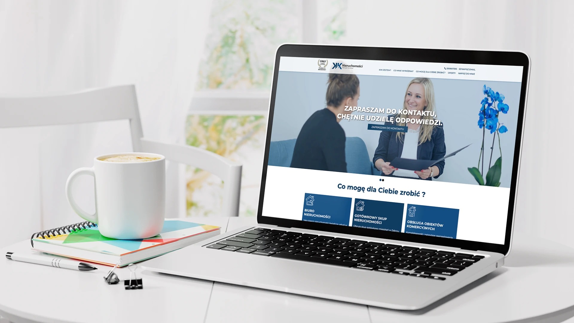 Laptop wyświetlający stronę internetową firmy z branży nieruchomości na biurku z kawą i notatnikiem w jasnym, minimalistycznym otoczeniu.