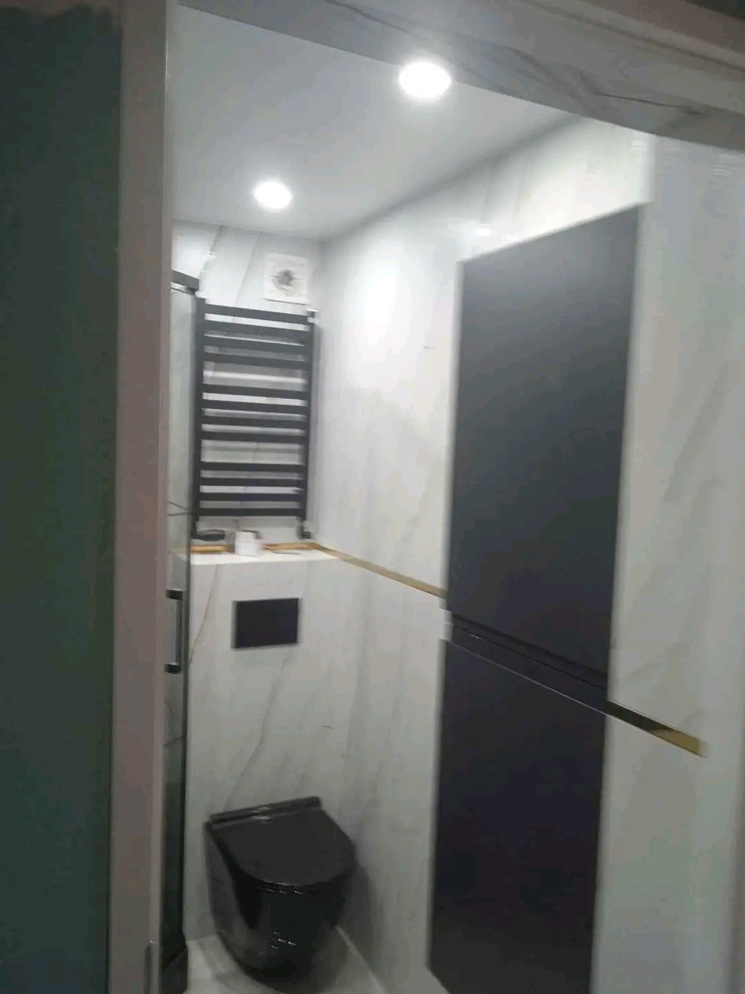 Wykończona łazienka w Kielcach z czarną toaletą i grzejnikiem drabinkowym na tle marmurowych płytek, widok zza framugi drzwi.