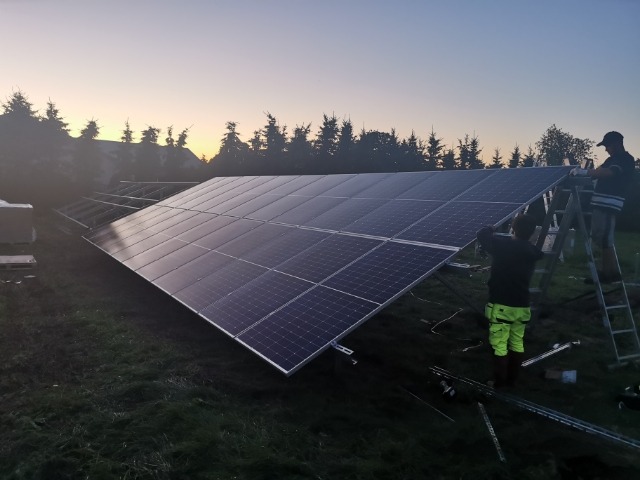 Montaż paneli na konstrukcji wsporczej przez dwóch instalatorów na tle zachodzącego słońca.