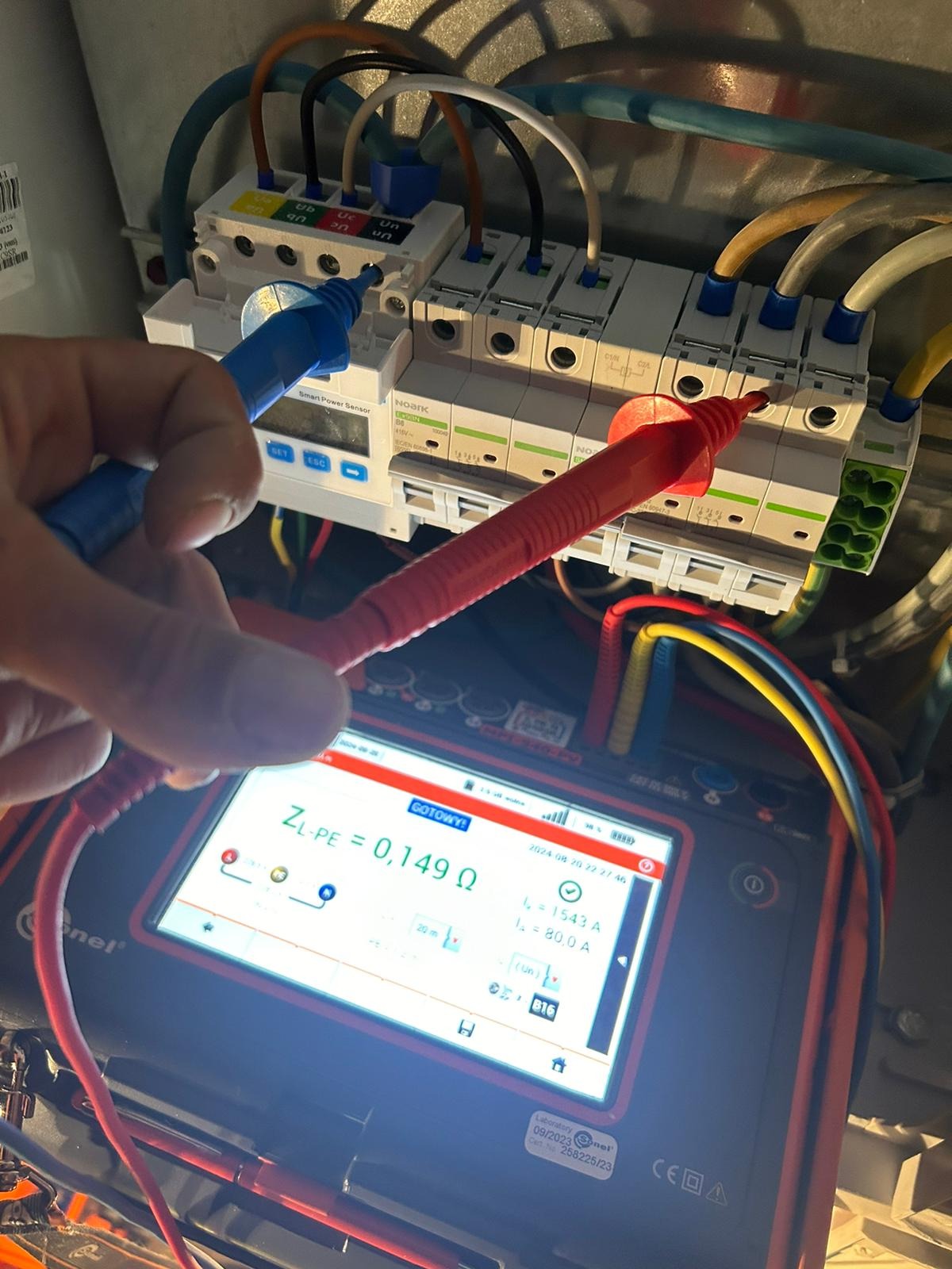 Pomiar impedancji pętli zwarcia ZL-PE 0,149 Ω na zabezpieczeniach różnicowoprądowych NOARK za pomocą miernika Sonel, widoczne przewody instalacji elektrycznej.
