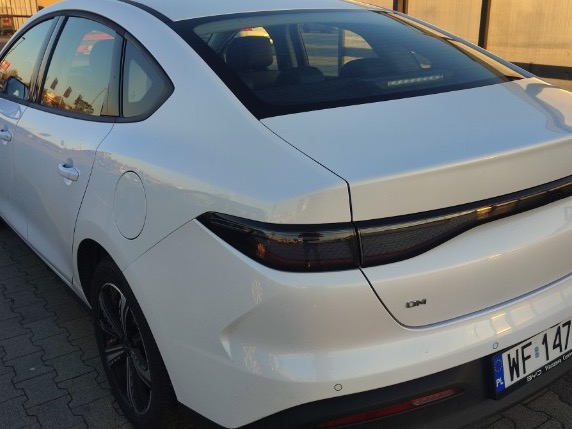 Biały samochód osobowy marki BYD z czarnymi lampami, widok z tyłu, tablica rejestracyjna WF 147. Auto zaparkowane na kostce brukowej.