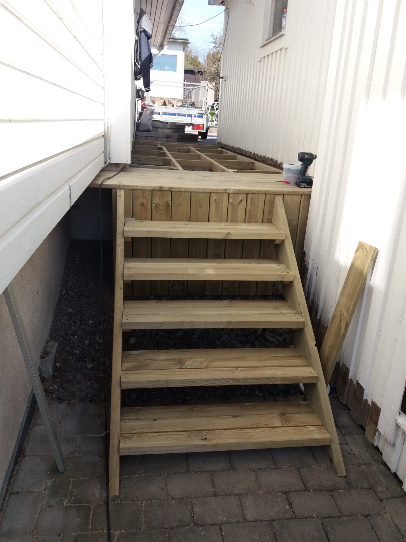 Drewniane schody prowadzące na częściowo zbudowany taras, widoczne narzędzia i materiały budowlane w tle.