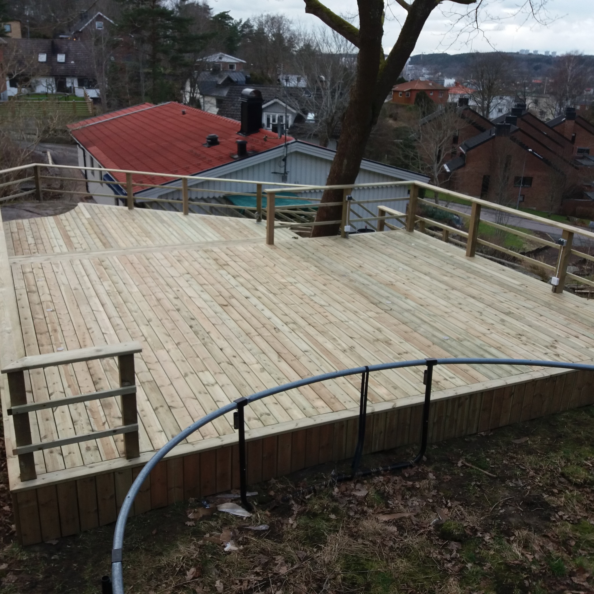 Nowy, drewniany taras z balustradami, zbudowany na zboczu, z widokiem na domy w tle.