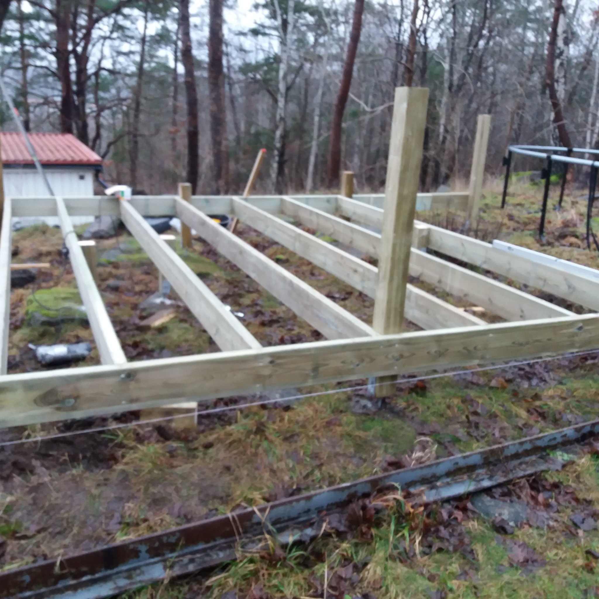Konstrukcja nośna z belek i słupów, prawdopodobnie pod przyszły taras, widoczna na zewnątrz w naturalnym otoczeniu leśnym, z elementami podłoża przygotowanymi pod budowę.