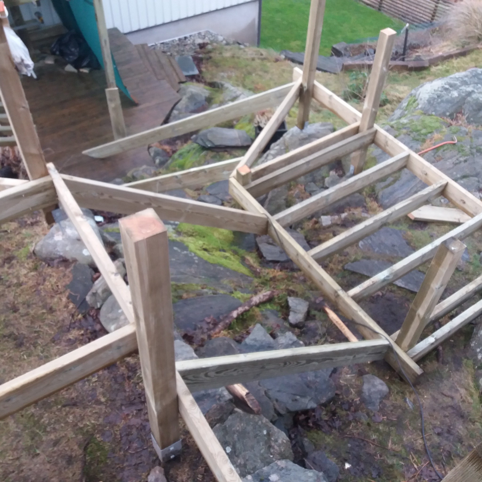 Szkielet drewnianej konstrukcji, prawdopodobnie tarasu, w trakcie budowy na nierównym, skalistym terenie.