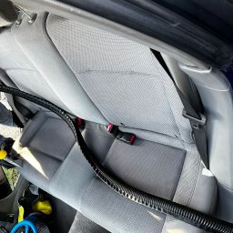 Nadiia Hirchytsia NaMi-Clean - Szary fotel samochodowy z widocznym przewodem odkurzacza piorącego i niebieskim wentylatorem do osuszania tapicerki.