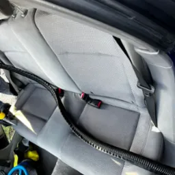 Szary fotel samochodowy z widocznym przewodem odkurzacza piorącego i niebieskim wentylatorem do osuszania tapicerki.