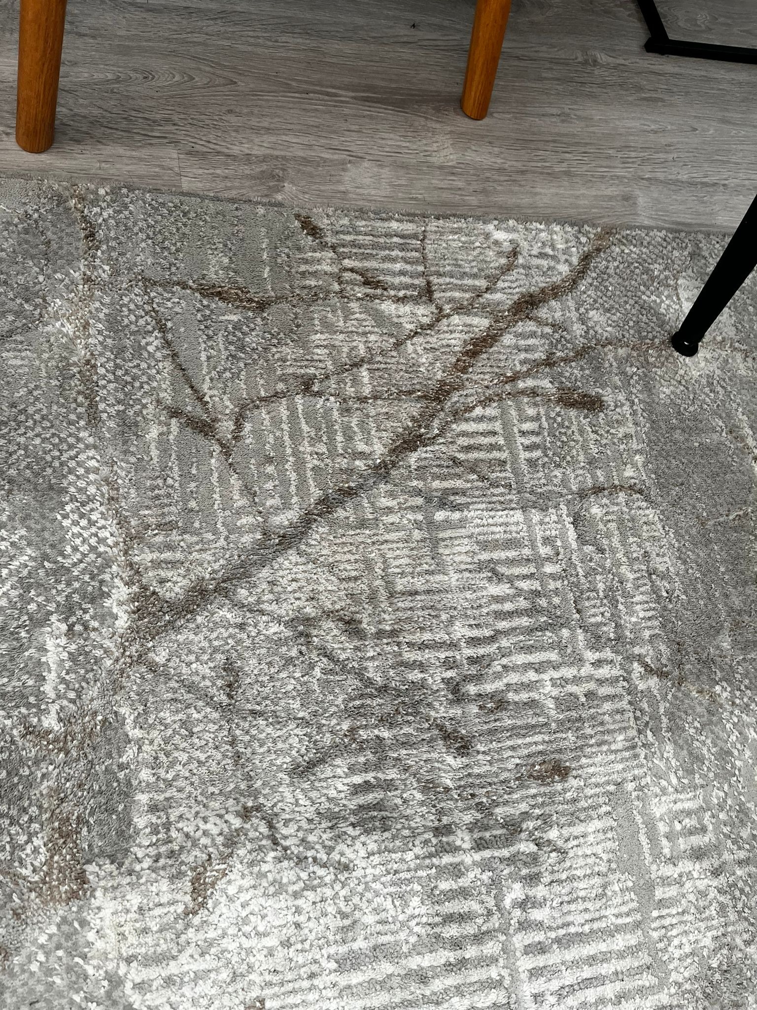 Szary dywan z geometrycznym wzorem, widoczne plamy i nogi krzeseł na tle podłogi z paneli.