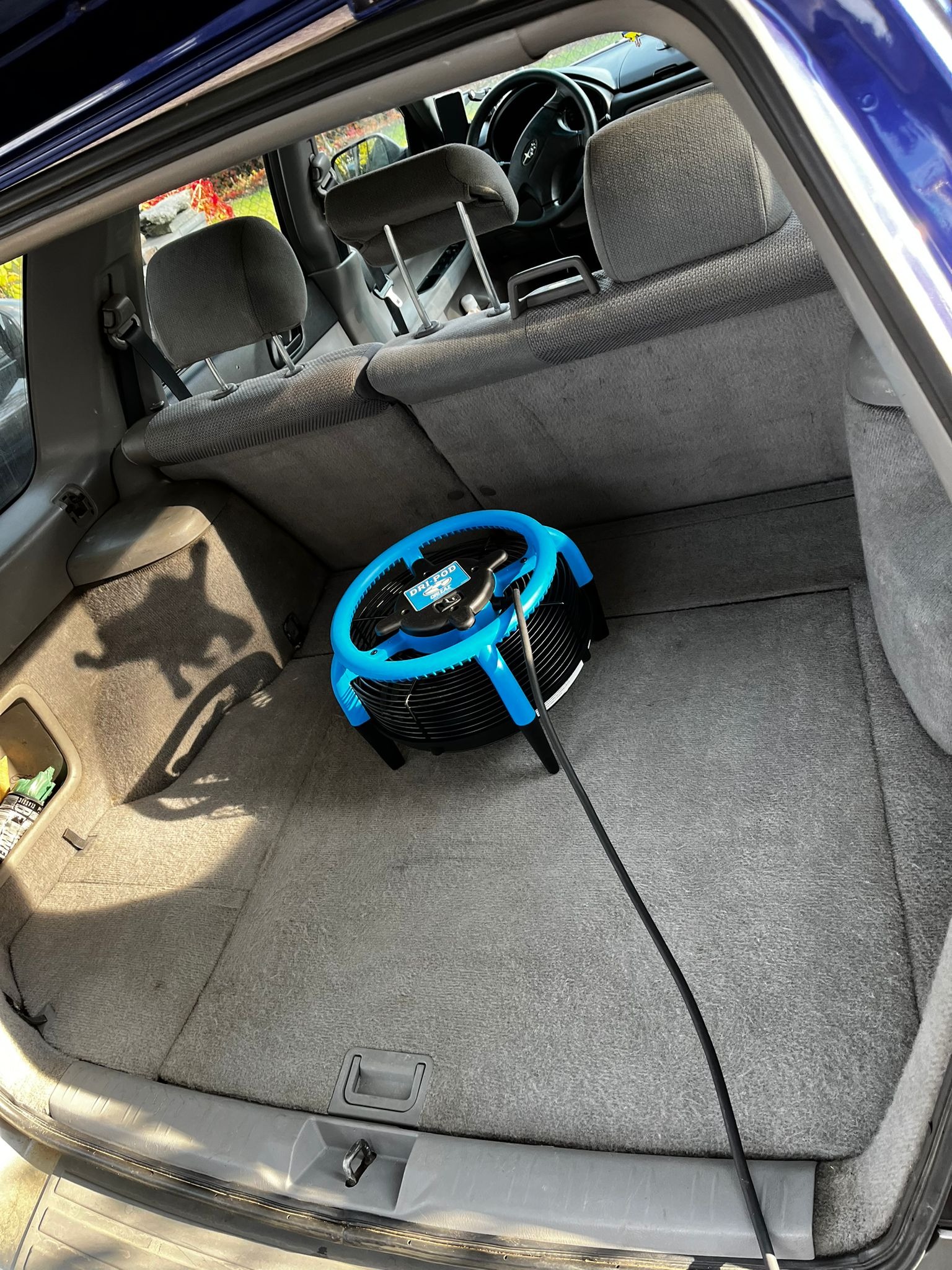 Wnętrze bagażnika samochodu w Opolu po praniu, z widocznym profesjonalnym wentylatorem osuszającym Dry Pod w kolorze niebiesko-czarnym, stojącym na szarej tapicerce.