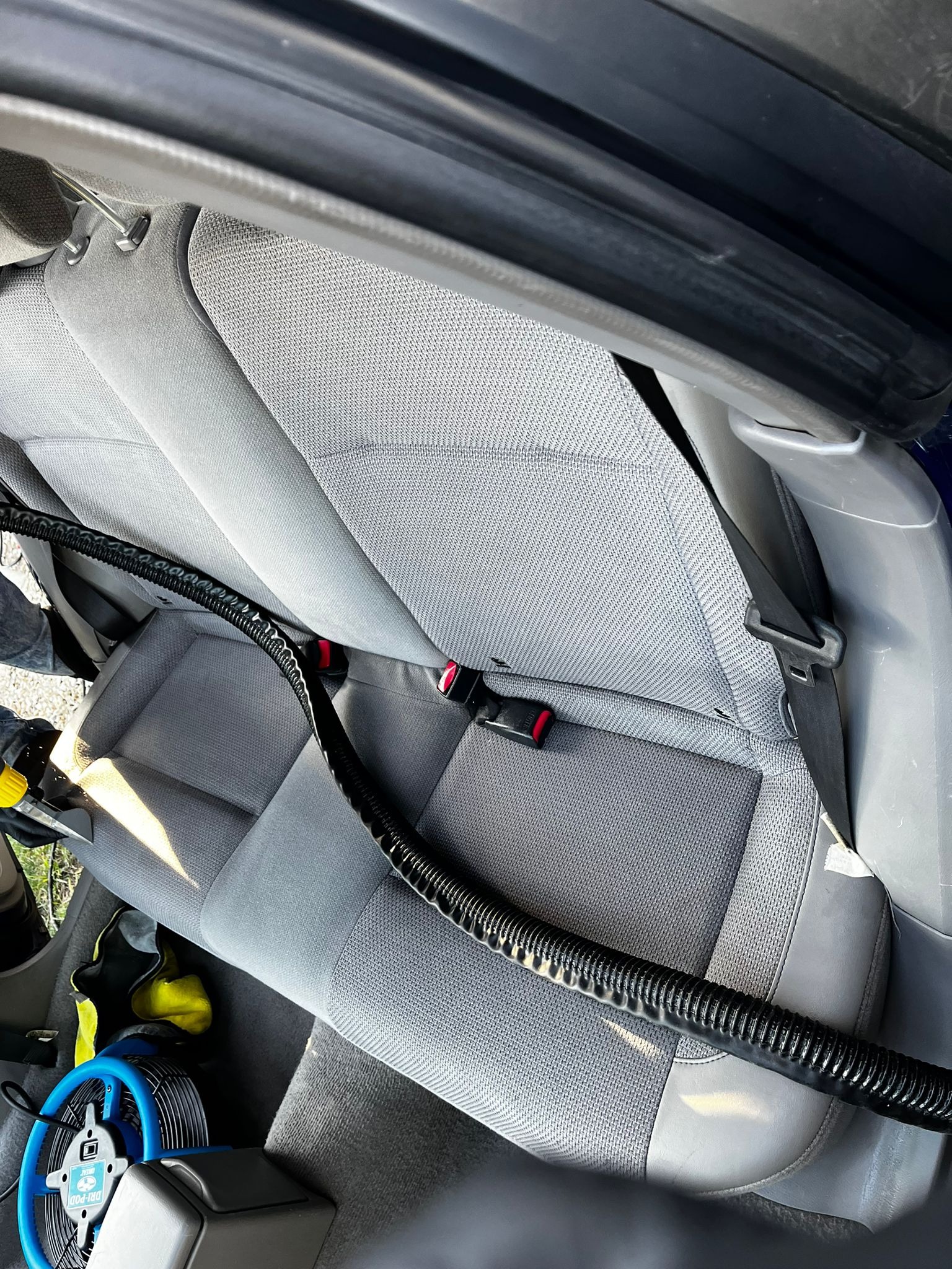 Szary fotel samochodowy z widocznym przewodem odkurzacza piorącego i niebieskim wentylatorem do osuszania tapicerki.