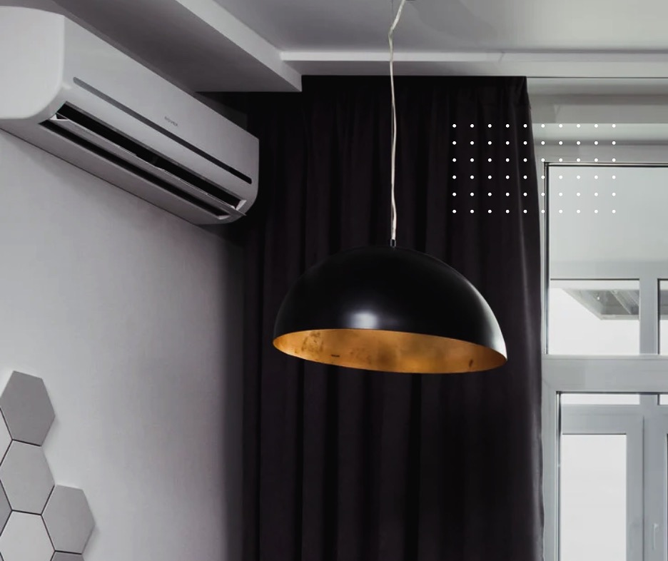 Biały klimatyzator ścienny w nowoczesnym wnętrzu, z czarną lampą wiszącą i dekoracyjnymi panelami heksagonalnymi na ścianie.