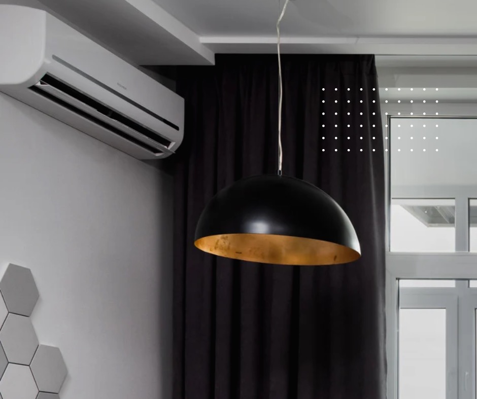 Biały klimatyzator ścienny w nowoczesnym wnętrzu z czarnymi zasłonami, sześciokątnymi płytkami na ścianie i czarną lampą wiszącą z złotym wnętrzem klosza.