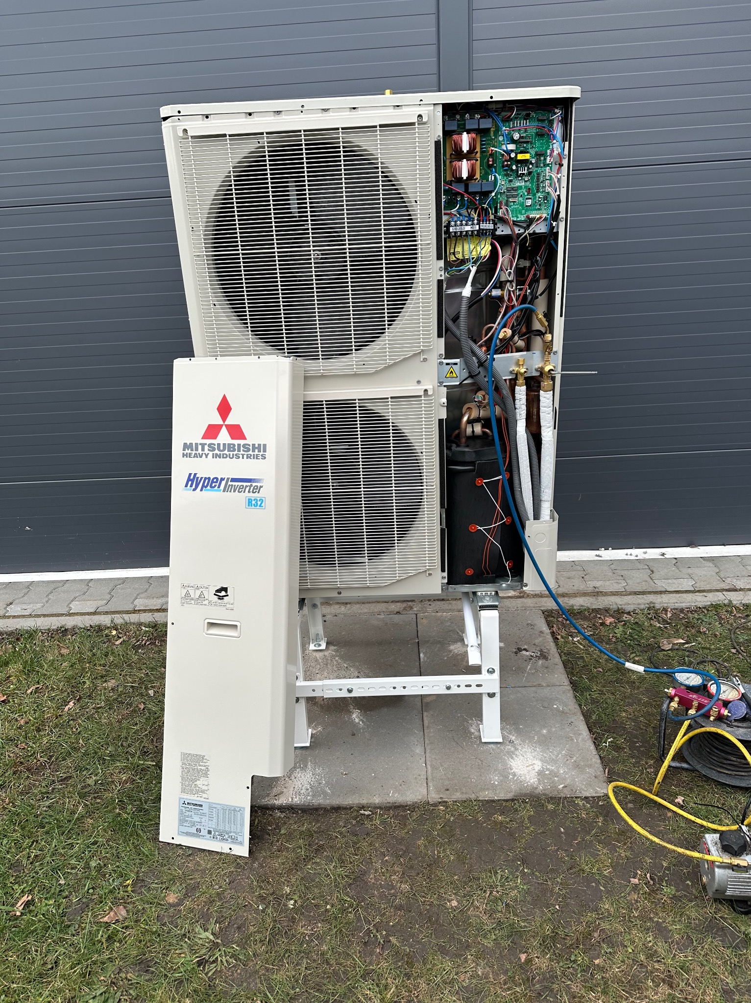 Otwarta obudowa zewnętrznej jednostki klimatyzacyjnej Mitsubishi Hyper Inverter R32 z widocznymi elementami wewnętrznymi i podłączonymi przewodami serwisowymi do diagnozy i uzupełniania czynnika...