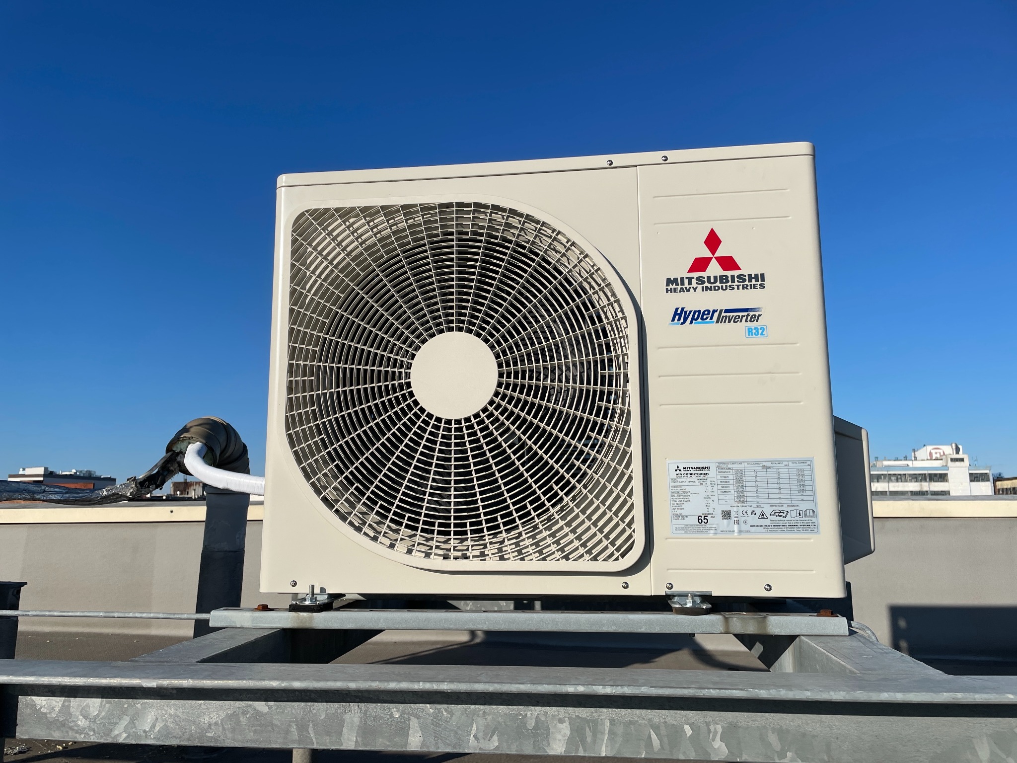 Zewnętrzna jednostka klimatyzacji Mitsubishi Heavy Industries na dachu budynku, zamontowana na metalowej konstrukcji, na tle błękitnego nieba.