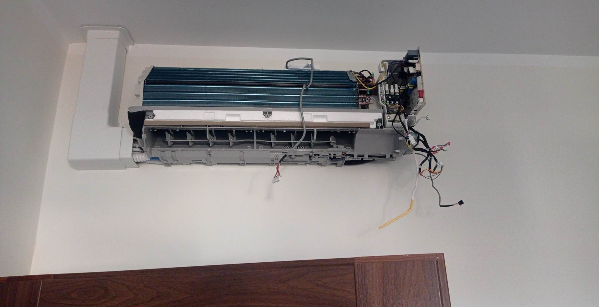 Rozmontowana jednostka wewnętrzna klimatyzatora na ścianie, widoczne przewody i elementy konstrukcyjne, dolny panel zdjęty, prawdopodobnie w trakcie czyszczenia lub naprawy.