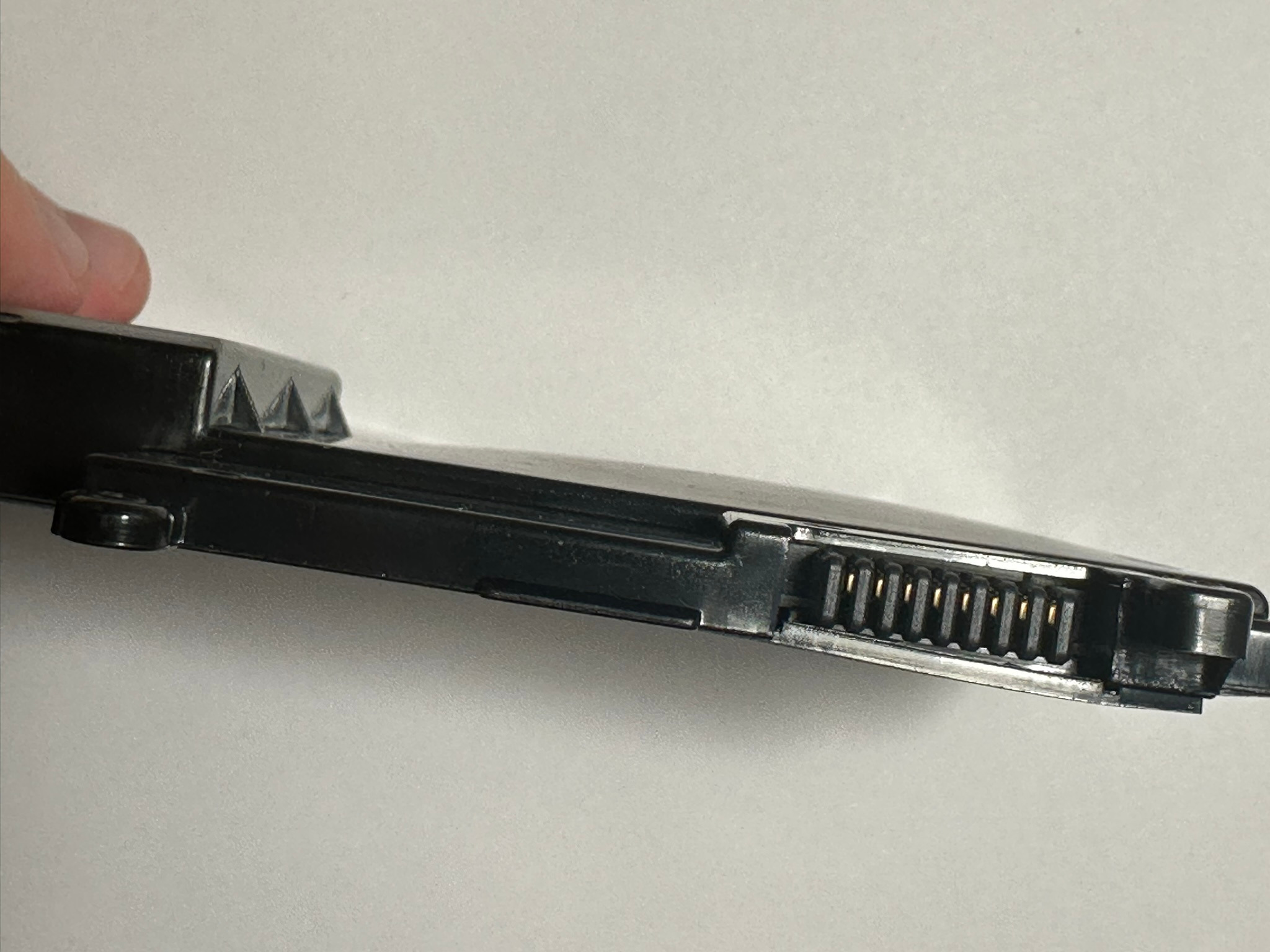 Czarny akumulator laptopa z widocznymi złotymi pinami złącza na jasnym tle, ukazujący detal i precyzję wykonania.