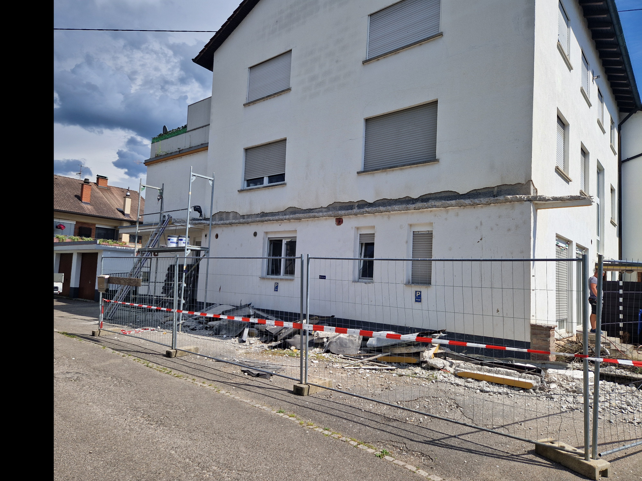 Demontaż ocieplenia budynku wielorodzinnego, widoczne rusztowania, gruz i tymczasowe ogrodzenie z siatki.