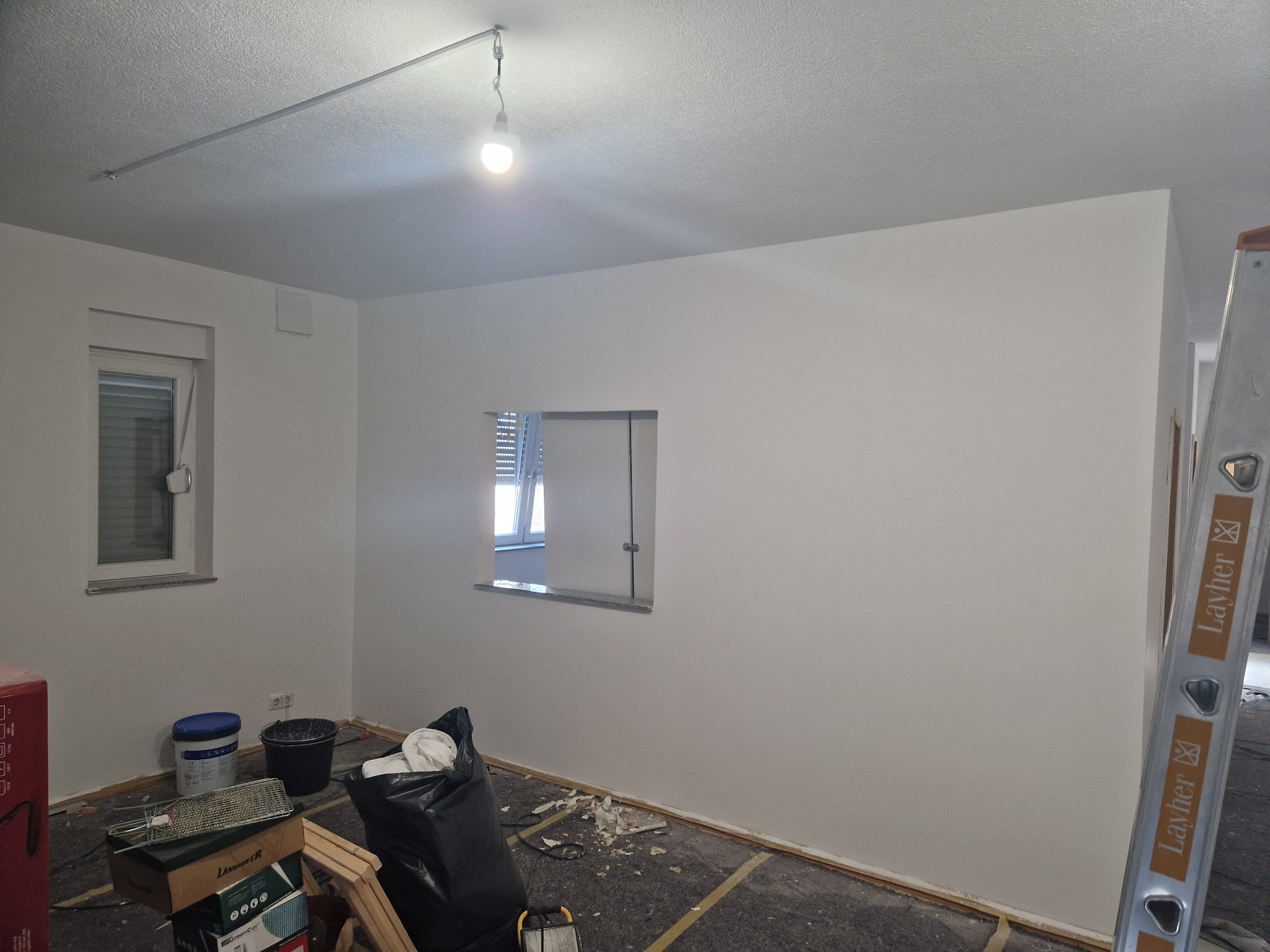 Wnętrze pokoju po szpachlowaniu ścian, widoczne narzędzia malarskie, wiadro z farbą i drabina Layher.