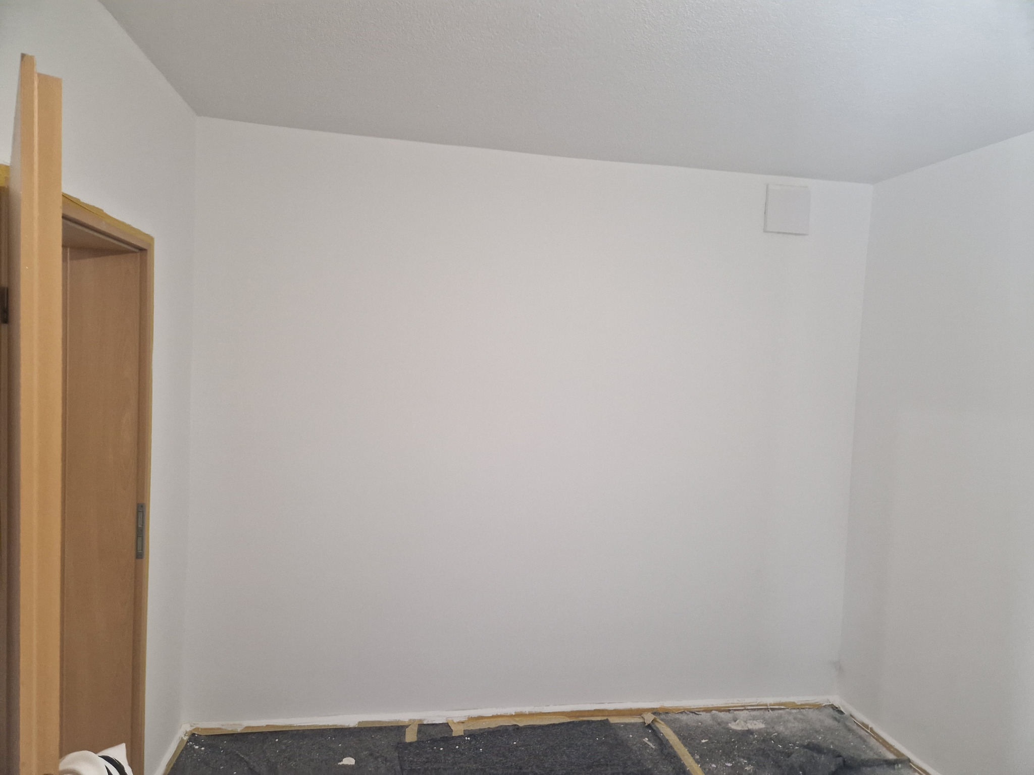 Pomalowane na biało wnętrze pokoju w trakcie remontu, widoczne przygotowane podłoże pod panele lub parkiet, oraz fragment ościeżnicy drzwiowej.